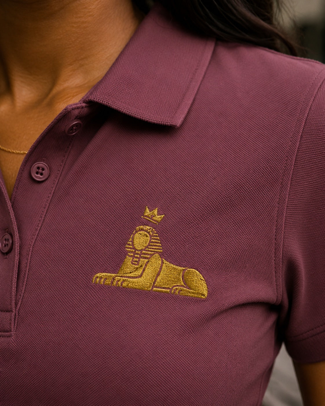 BLACK MAJIC Women's Crown Polo in Rosewood, close view of the gold embroidered crowned Sphinx