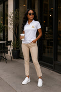 Black woman wearing the BLACK MAJIC Women's Crown Polo in White on a city street, gold embroidered crowned Sphinx at the left chest