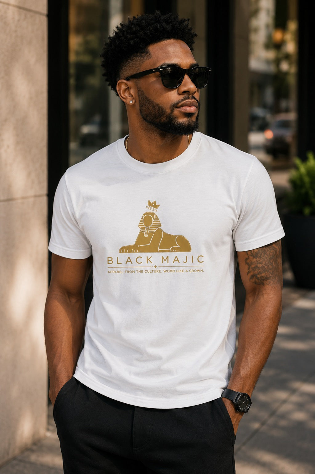 Black man wearing the BLACK MAJIC Crown Graphic Tee in white, filled gold crowned Sphinx over the wordmark