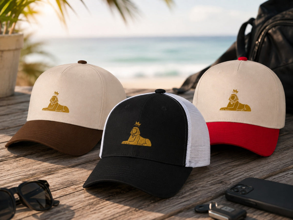 BLACK MAJIC caps on a weathered wood table by the water — natural five-panel and black and red truckers