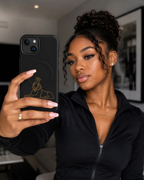 Black woman holding a phone in the BLACK MAJIC MagSafe Tough Case in black, gold crowned Sphinx