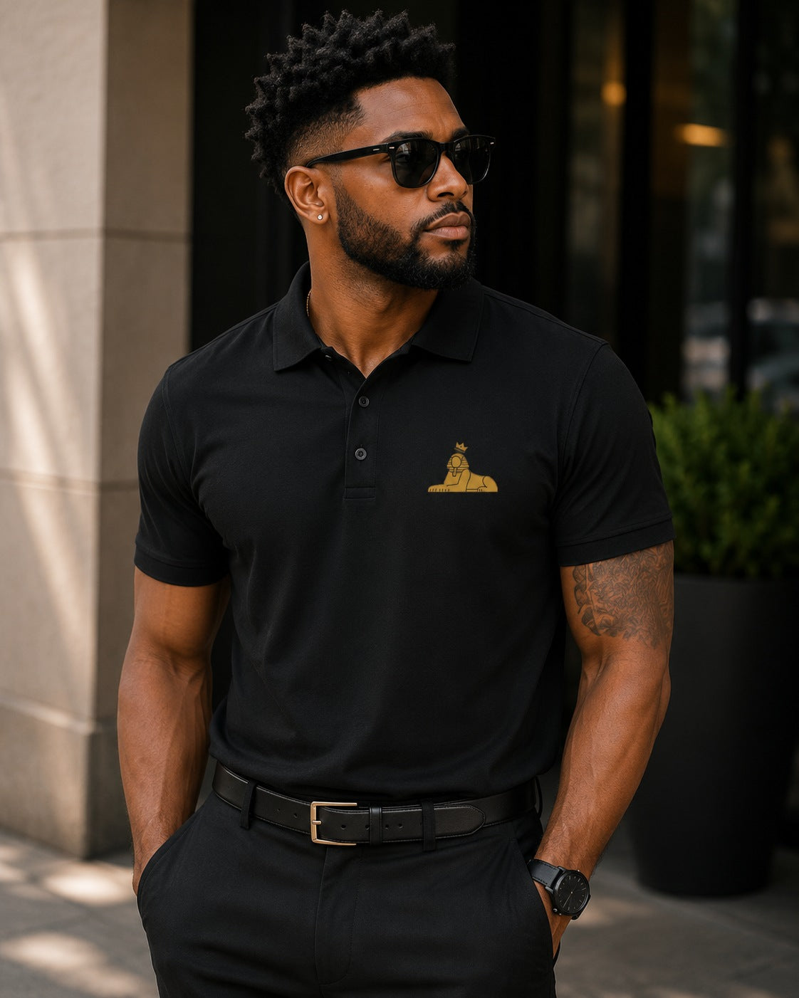 Black man wearing the BLACK MAJIC Adult Crown Polo in Black, gold embroidered crowned Sphinx at the left chest