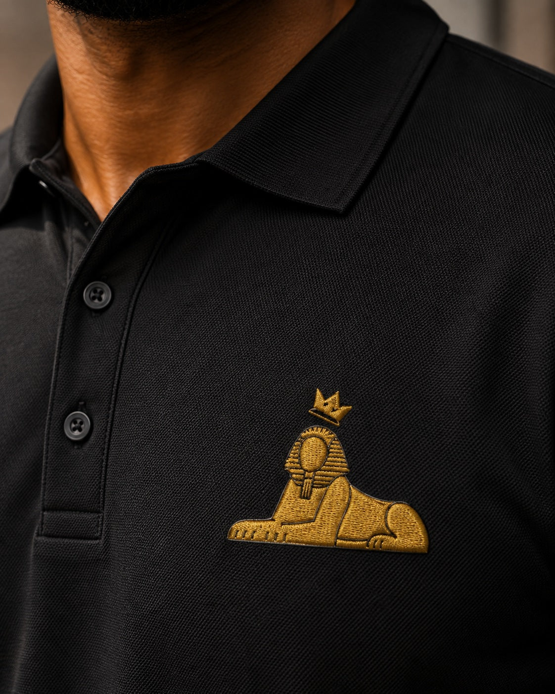 Close view of the gold embroidered crowned Sphinx on the BLACK MAJIC Adult Crown Polo in Black