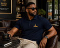 Black man wearing the BLACK MAJIC Adult Crown Polo in Sport Dark Navy, seated in a lounge
