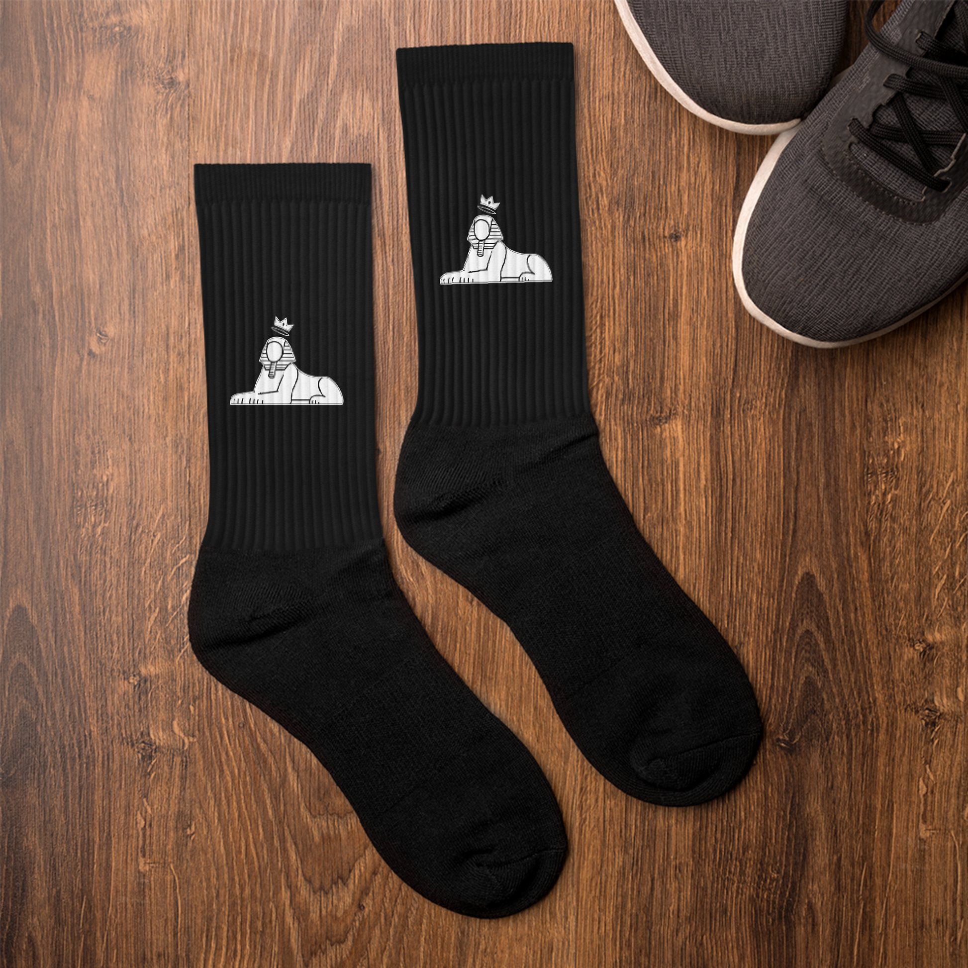 BLACK MAJIC Crown Socks in black laid on a wood floor beside sneakers