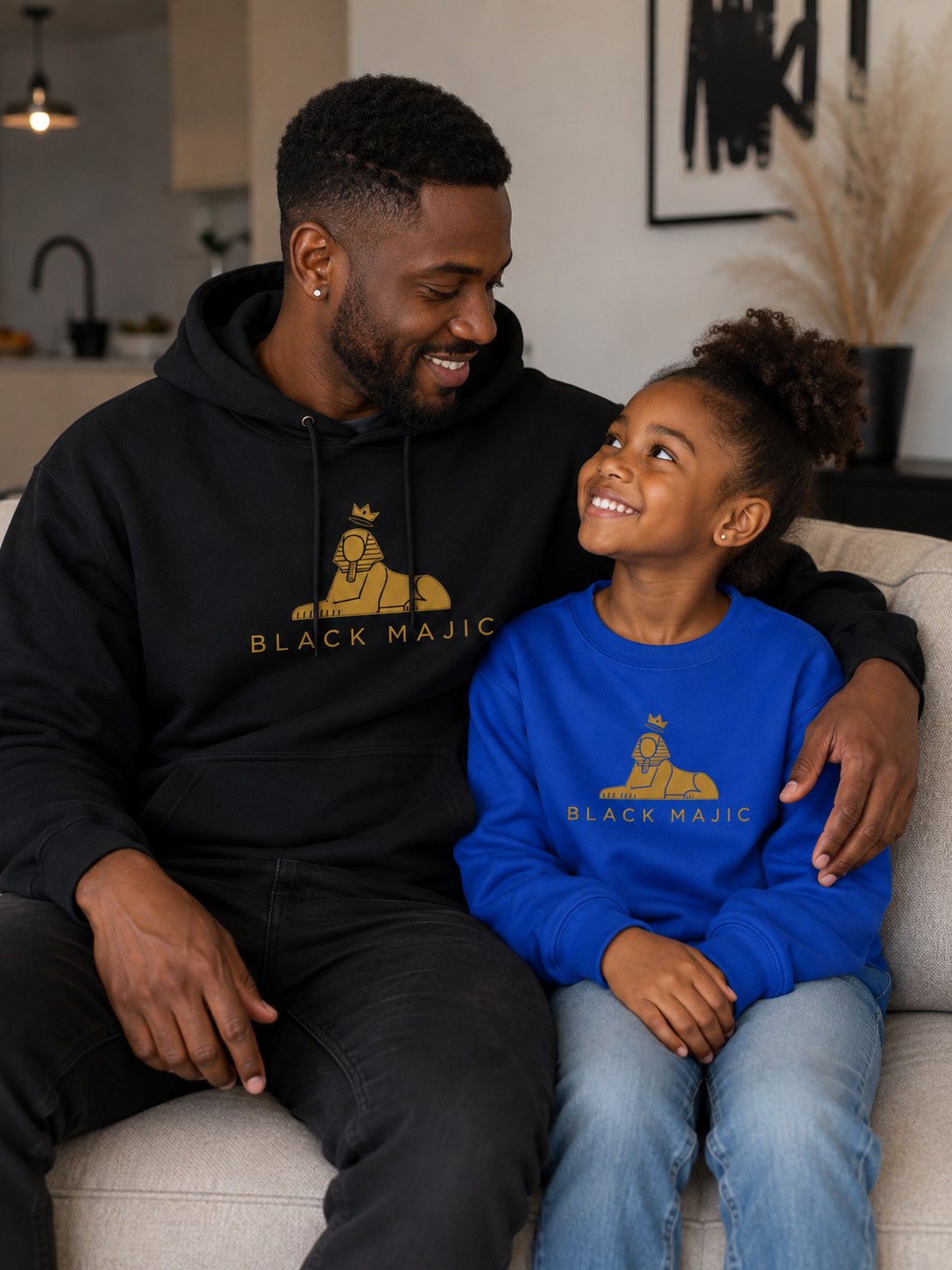 BLACK MAJIC Crown Hoodie in black on a father at home, gold crowned Sphinx over the wordmark across the chest