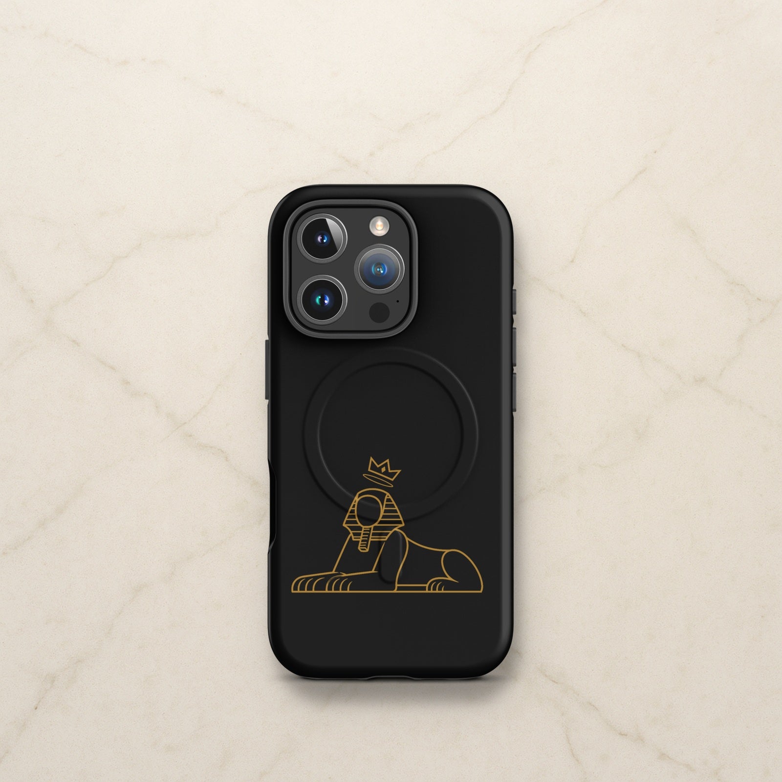 BLACK MAJIC MagSafe Tough Case in black with the gold crowned Sphinx, on a pale marble counter