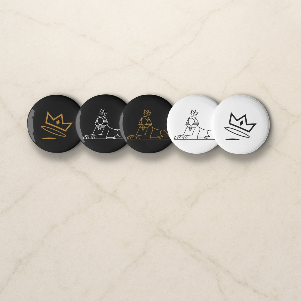BLACK MAJIC Pin Set, five crowned Sphinx and crown buttons in black and white on a pale marble counter