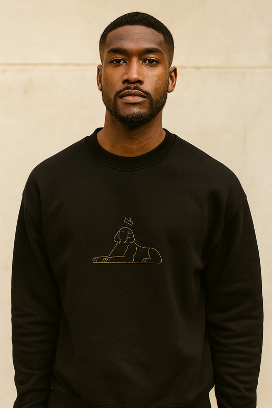 Black man in the black-on-black Embroidered Crewneck, tonal sphinx visible, bright daylight