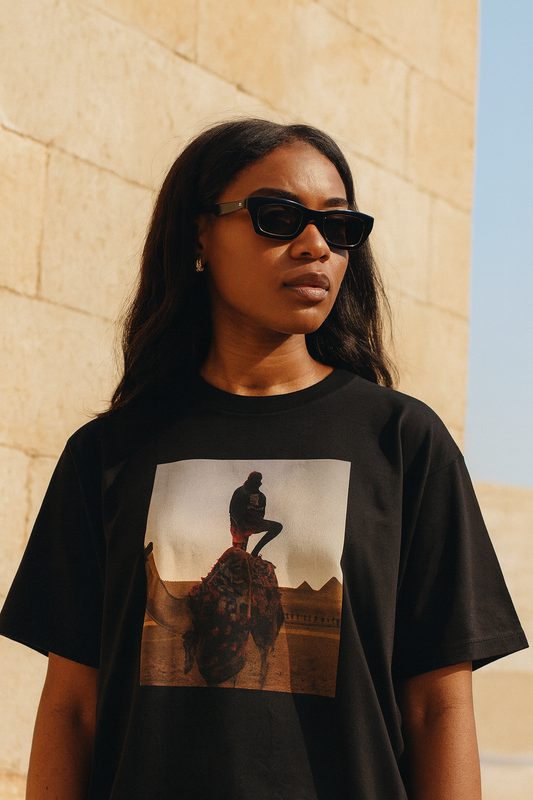 Black woman in the Velvet Ritual Giza Tee, bright daylight, light sandstone wall